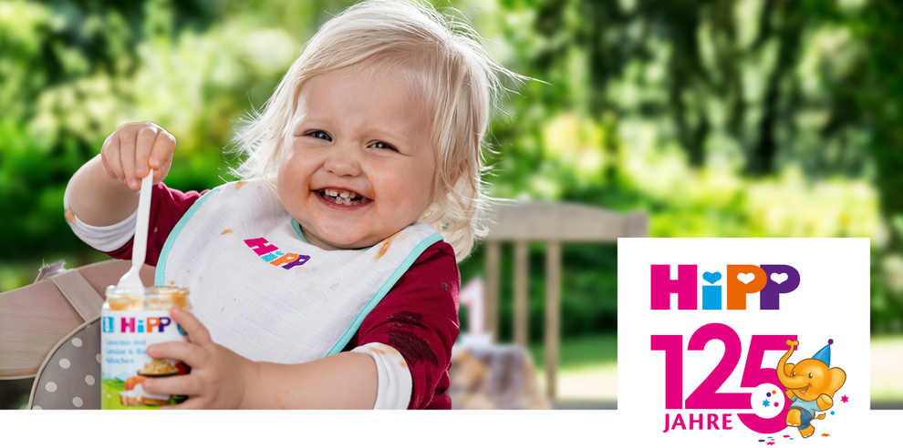 A joyful toddler with blonde hair is eating from a jar, with a logo and text celebrating "HiPP 125 Jahre" on the right.