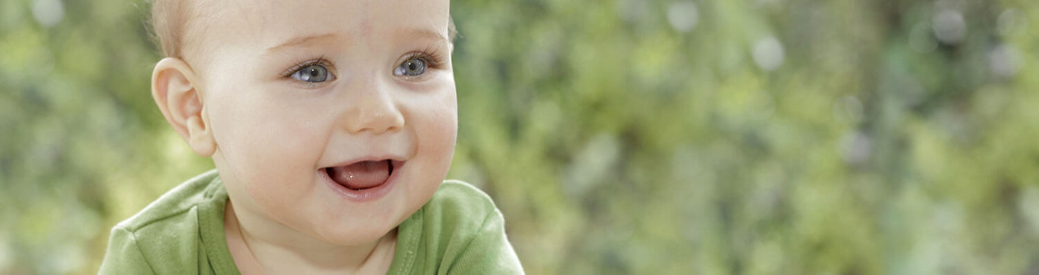 A baby with blue eyes and a green shirt is set against a blurred green background.