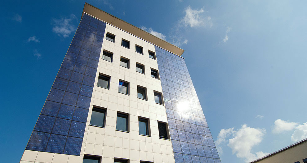 A modern building with a white and blue facade stands under a clear sky with a few clouds.