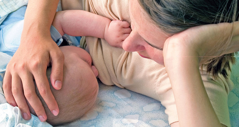 A woman cradles a baby's head on a patterned fabric.