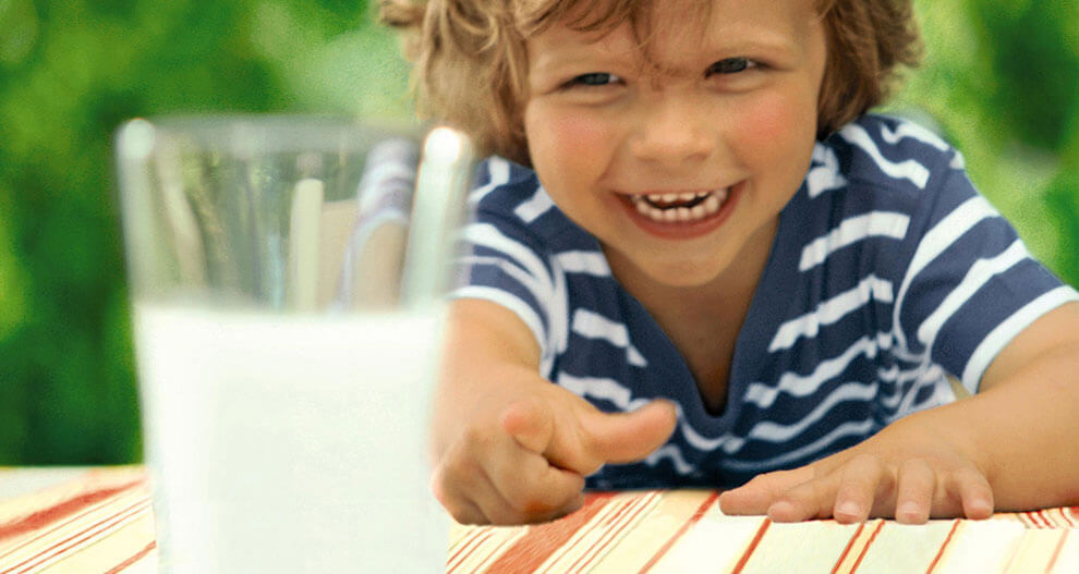 A child in a striped shirt is reaching out towards a glass of milk.