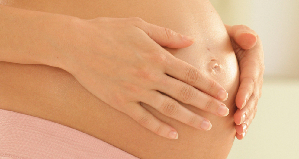 A pregnant woman's hands gently cradle her belly.