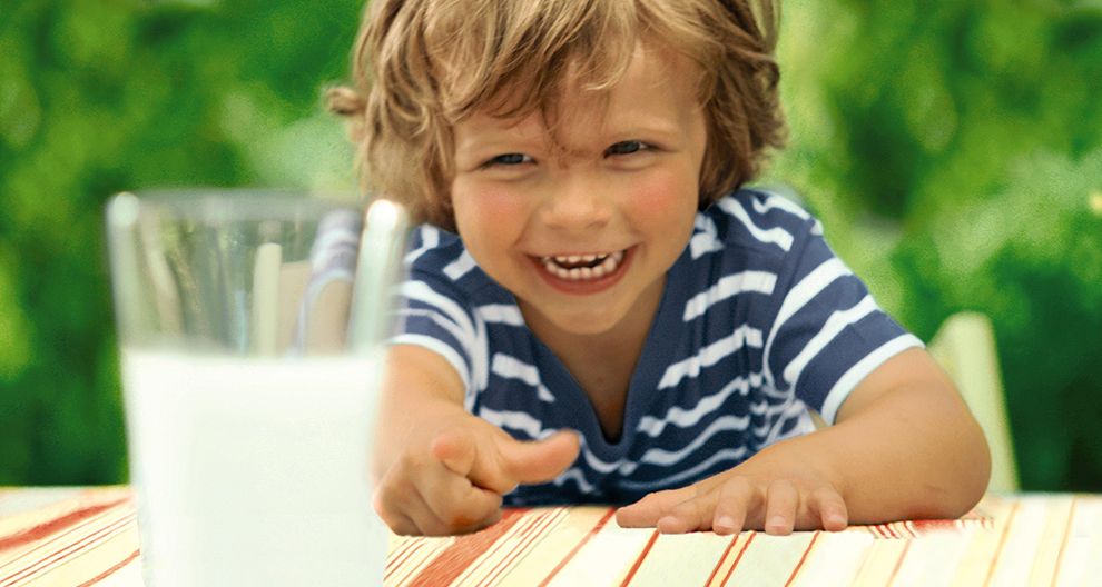 A child with a striped shirt is reaching out towards a glass of milk.