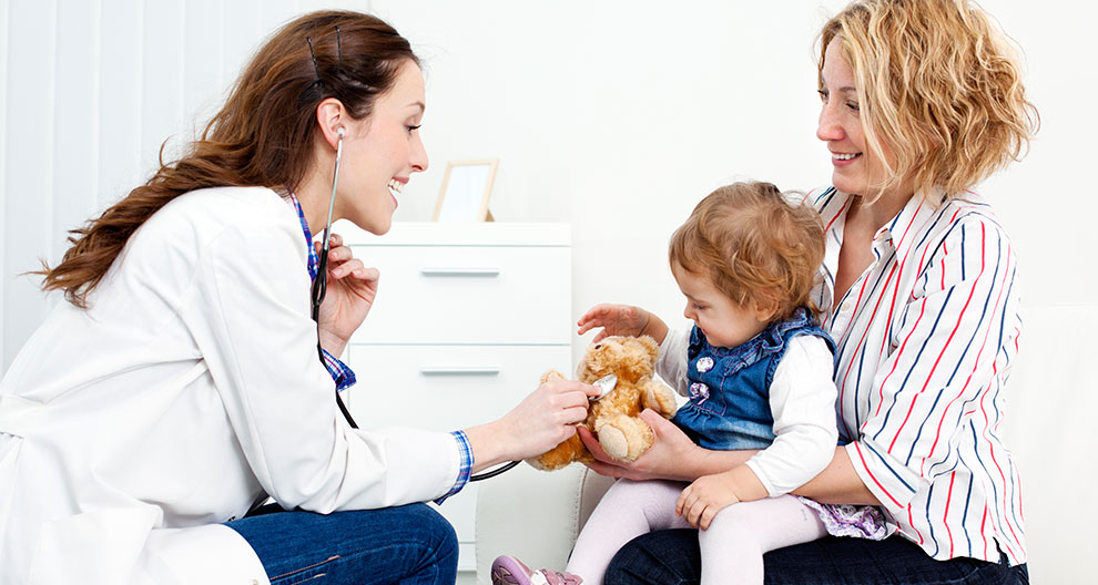 A healthcare professional interacts with a child and a woman in a clinical setting.