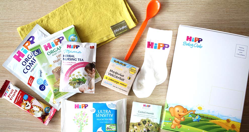 Različni izdelki in dodatki za dojenčke, vključno z žličko, nogavicami, čajem, robčki in škatlo HiPP Baby Club.
