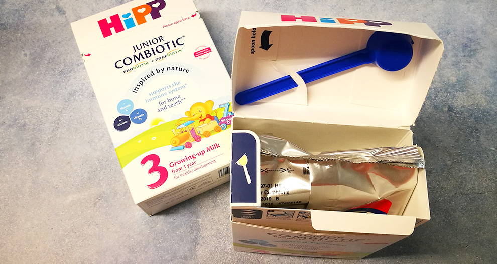 Škatla otroške formule Hipp Junior Combiotic Stage 3 z modro žličko in zaprto vrečko s praškom.