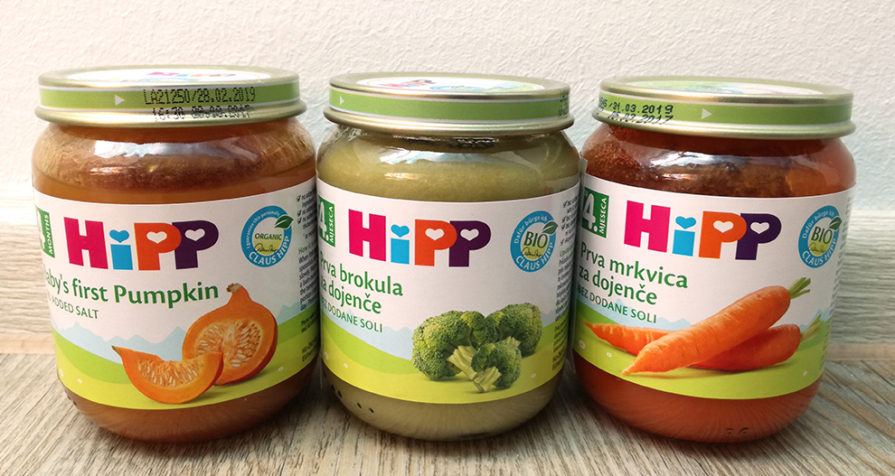 Trije stekleni kozarci z etiketami, na enem je ilustracija buče, na drugem brokolija, na tretjem korenčka, vse pod blagovno znamko "HiPP".