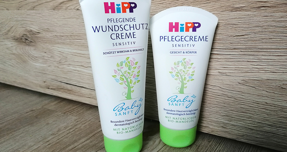 Dve tubi kreme z oznako "HiPP Pflegecreme SENSITIV Baby SANFT" položite na leseno površino.