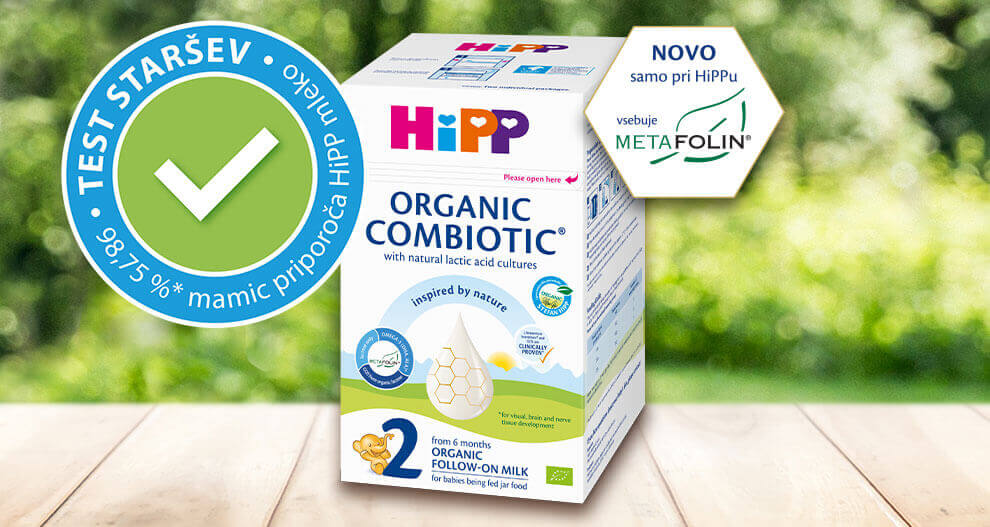 Na zamegljenem naravnem ozadju je prikazana škatla izdelka z oznako "HiPP Organic Combiotic" z zeleno kljukico "Test Starsev" in novim dodatkom "MetaFolin".